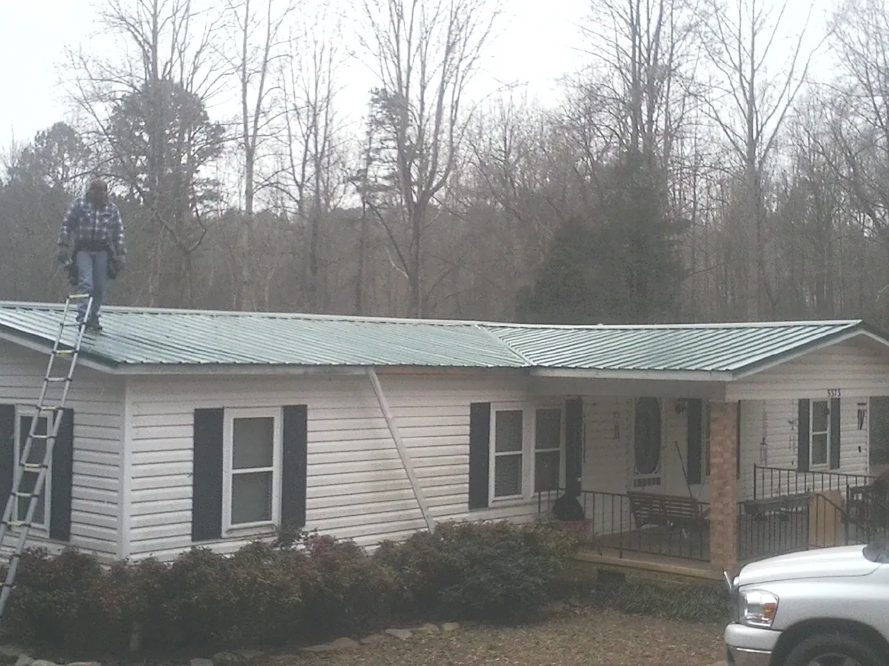 Worker on a ladder beside a new green metal roof on a ranch home in Jamieson