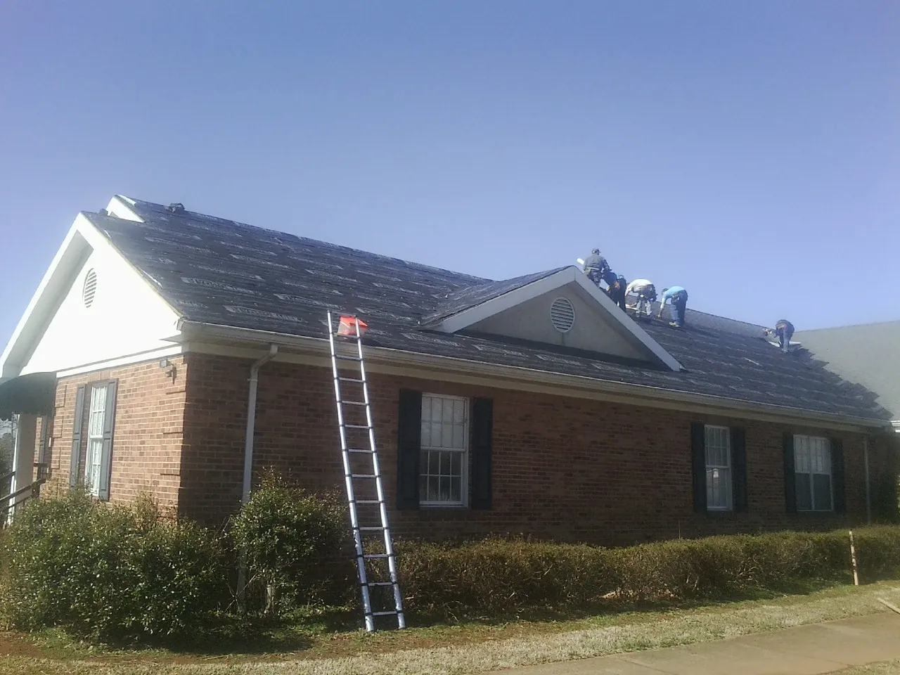 Crew tearing shingles off a brick ranch roof with a ladder set — Metal Roof Repair work by our crew in Jamieson