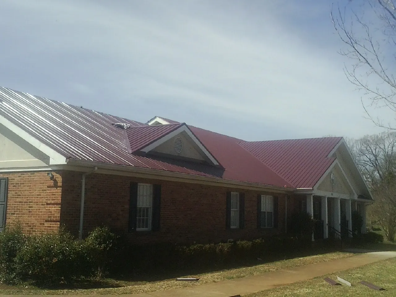 Red metal roof with gabled entries on a long brick building, from a Hail Damage Roof Repair job in Jamieson