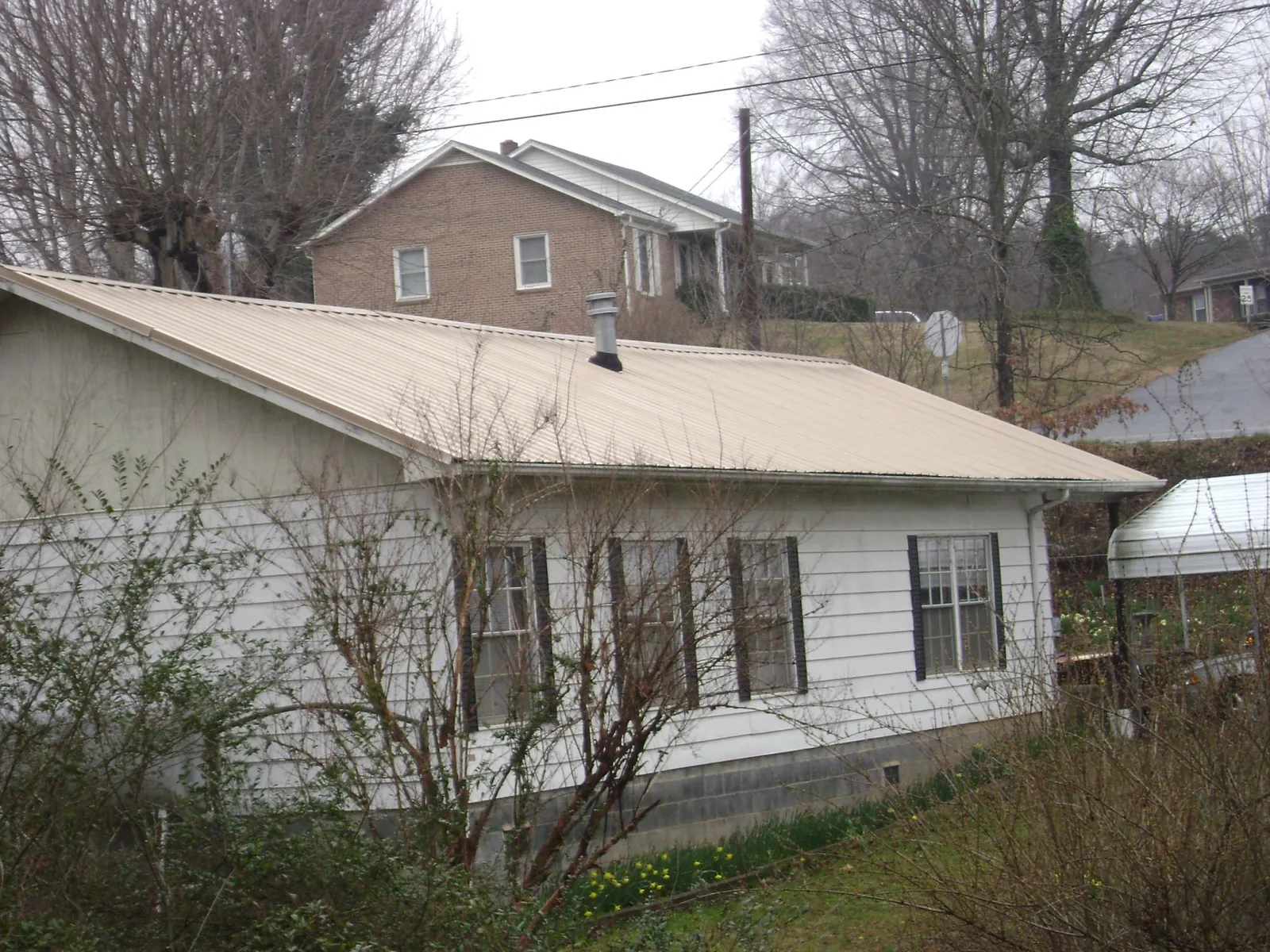 Tan metal roof on a white sided house set into a hillside — Commercial Roofing by Roofing Brothers in Jamieson